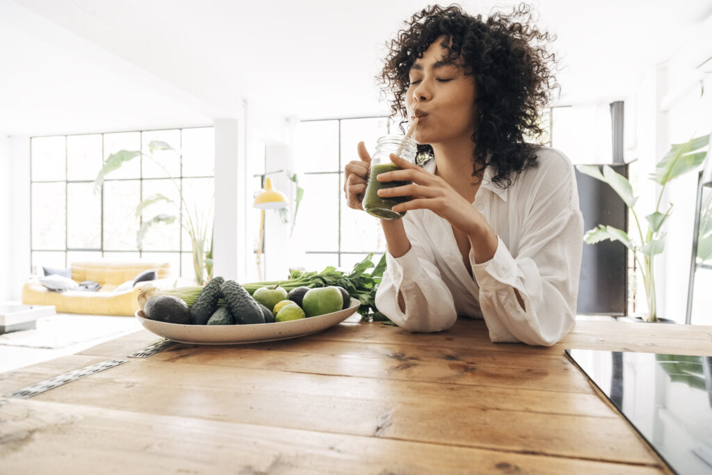 Young african american woman drinking green juice with reusable bamboo straw in loft apartment. Home concept. Healthy lifestyle concept. Copy space